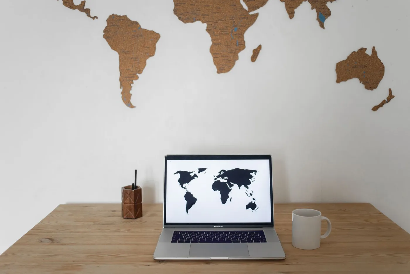 A world map above a desk with a laptop showing the globe