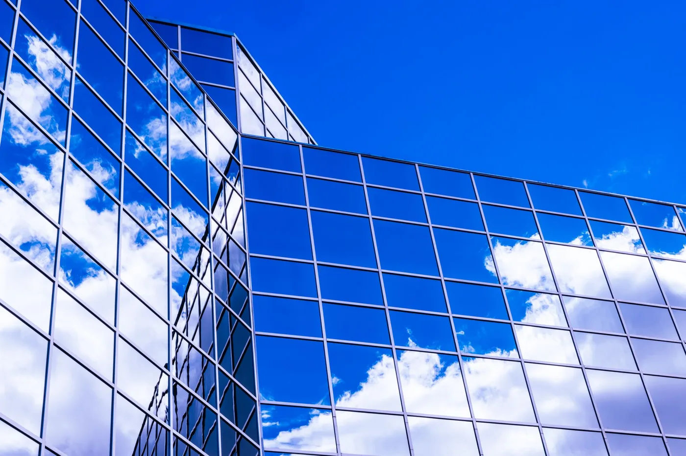 Blue glass curtain wall of an office building reflecting white clouds