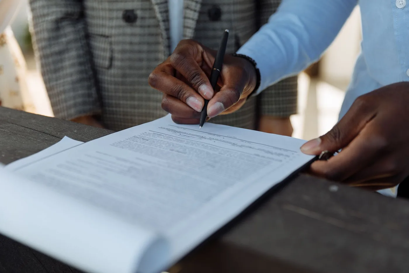 Signing a printed agreement across a meeting table