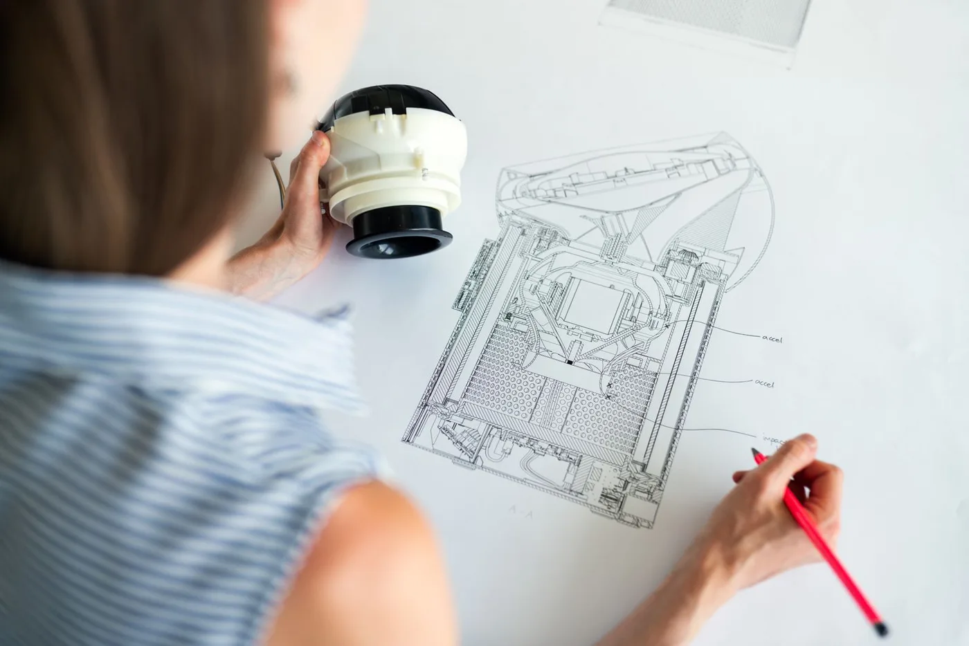 A loupe held over a technical drawing while a pencil marks it up